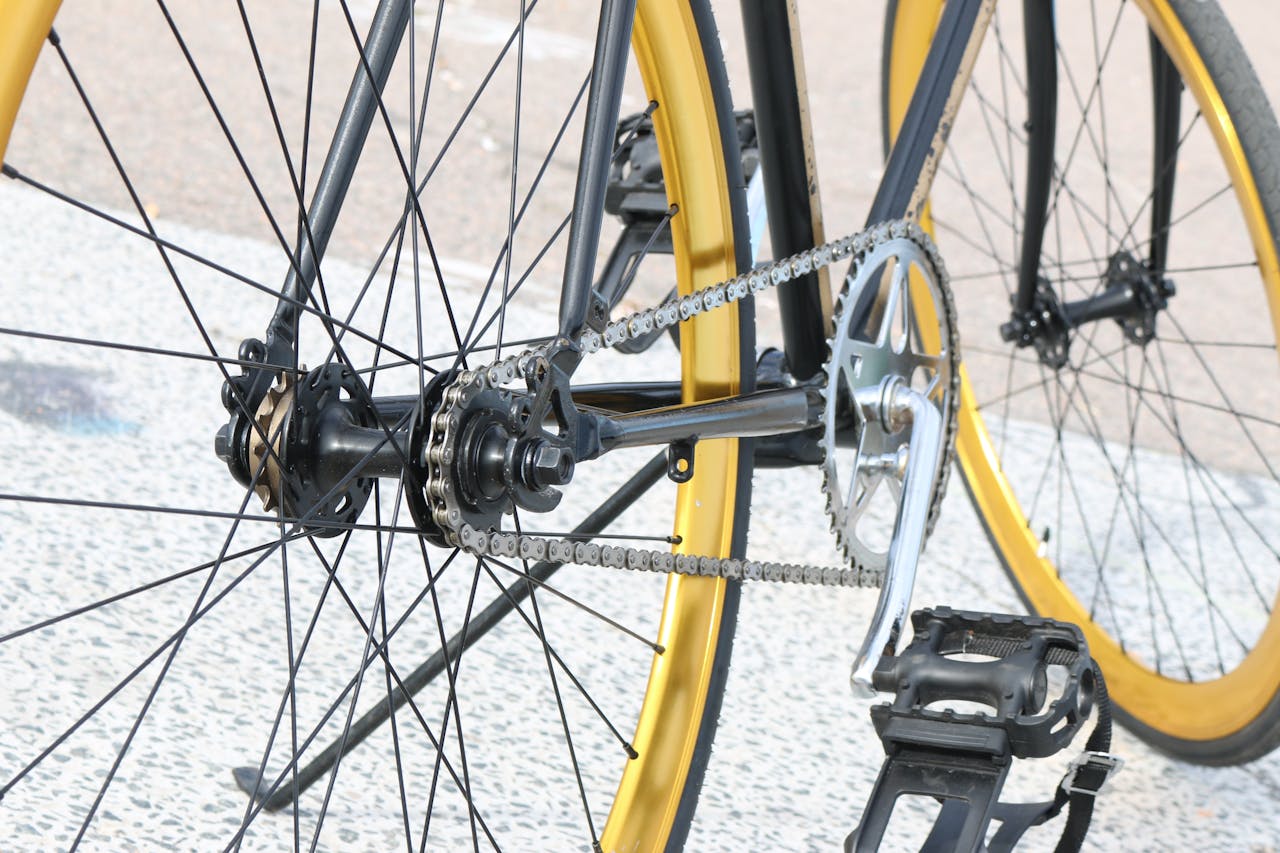 Detailed view of a bicycle chain and gear system with yellow rims in an urban setting.